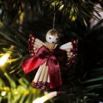 Close-up of a handmade Christmas angel ornament hanging on a festive tree branch.